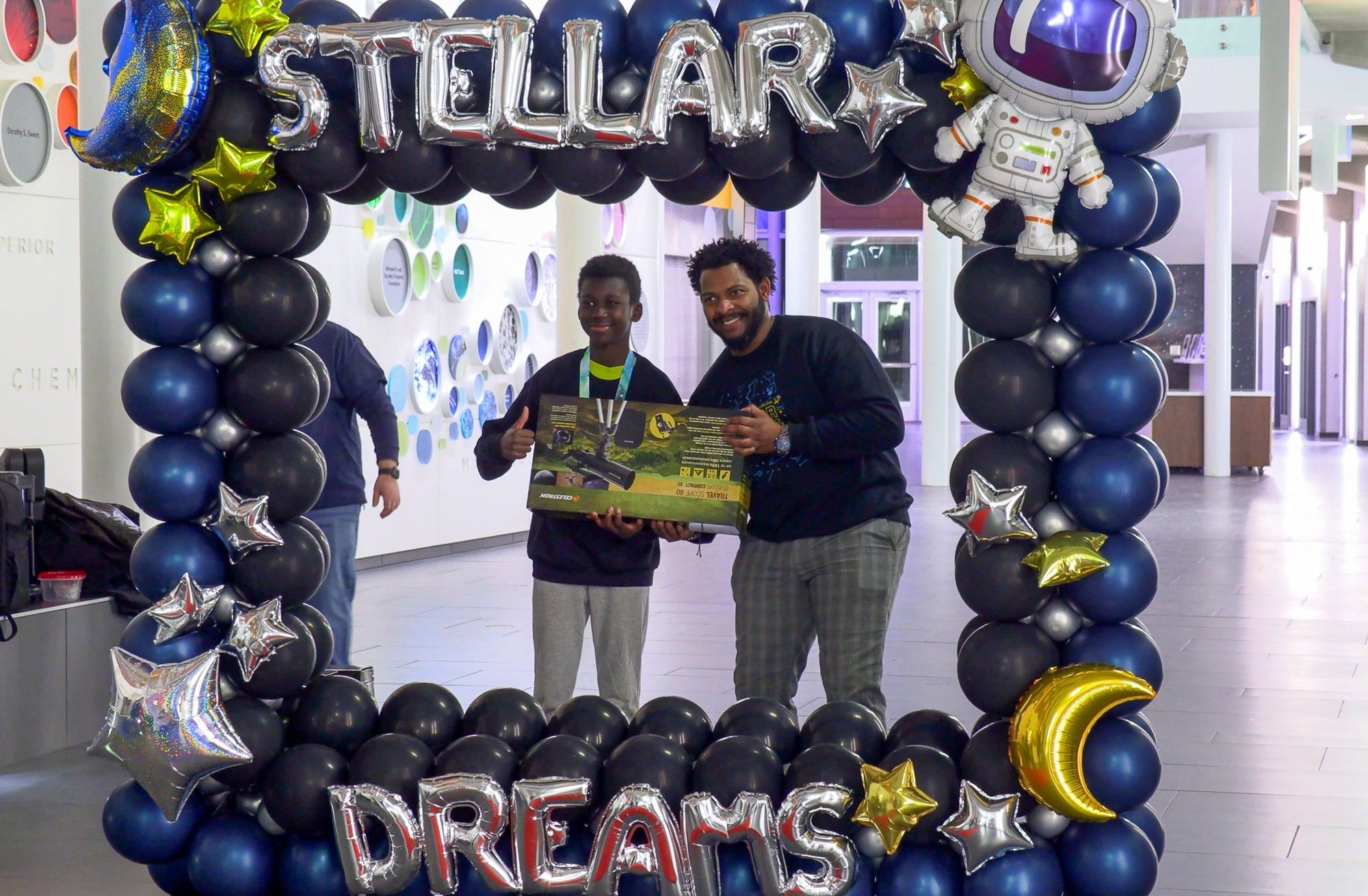 Students and their families hold new telescopes under the Stellar Dreams balloon arch