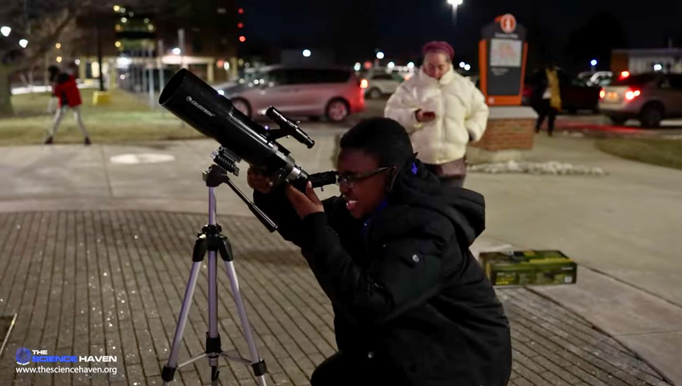 A student points a telescope at the night sky