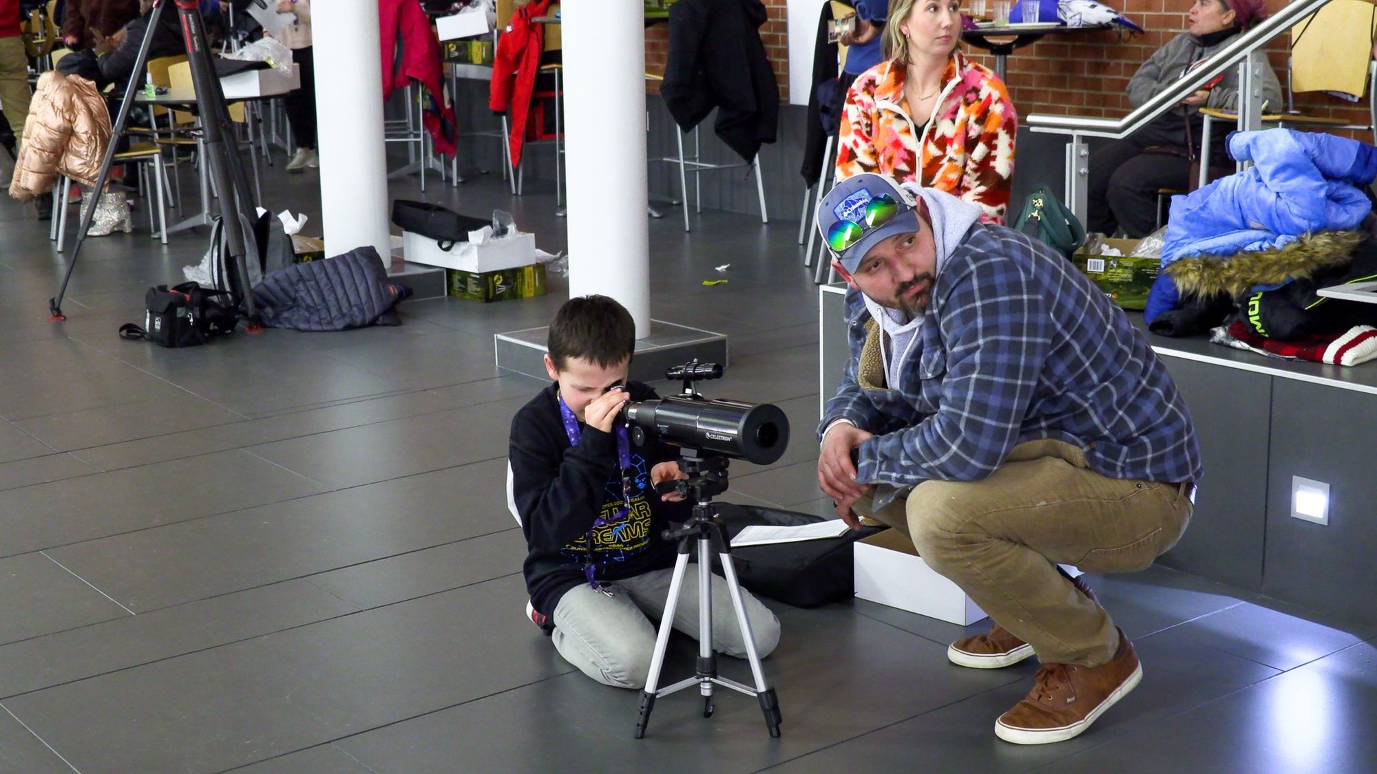 A student looks through a new telescope while a volunteer helps at the Stellar Dreams kickoff